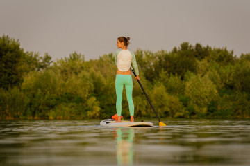 Fototapeta na wymiar Fit slim woman on paddleboard at sunset