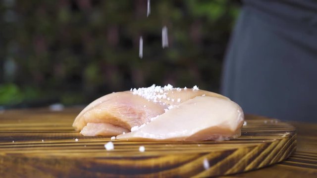 Raw fresh chicken fillet meat on wooden table close up. Salt pouring on chicken breasts lying on kitchen board. Process preparation healthy food. Fitness food and protein diet. Cooking meat dish.