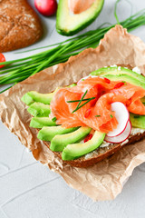 sandwich with avocado and salmon on a light background, green onions and gluten-free grain bread, radishes and tomatoes. concept diet food, copy space, sandwich take away, healthy fast food
