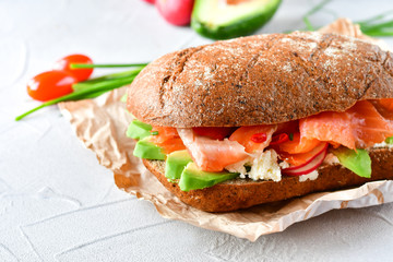 sandwich with avocado and salmon on a light background, green onions and gluten-free grain bread,...