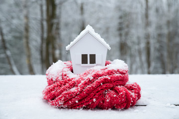 house in winter - heating system concept and cold snowy weather with model of a house wearing a knitted cap