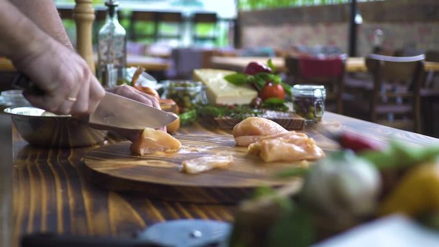 Chef Cook Slicing Fresh Chicken Breasts With Knife On Wooden Table. Slow Motion Cutting Chicken Fillet On Slices. Cooking Food On Kitchen Close Up. Fitness Food, Healthy Nutrition, Low Calorie Diet.