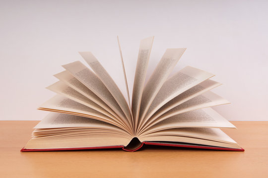 open hardcover book with turning pages in fan shape on desk                              