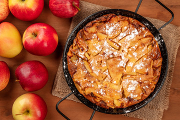 A closeup photo of an apple pie in a pan, shot from the top on a dark rustic wooden background with...