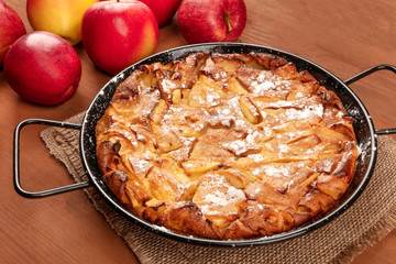 A photo of an apple pie in a pan, on a dark rustic wooden background with heirloom apples
