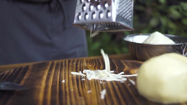 Grating cheese on grater close up. Chef cook grating fresh cheese for preparation food mediterranean cuisine. Ingredients for italian pizza or greek salad. Process cooking food on kitchen.