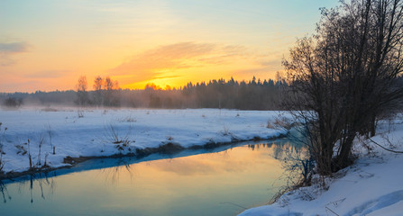 Obraz premium Frosty foggy winter landscape with small forest river and rising sun.