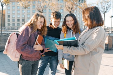 Mature female teacher talking to teenage students outside of school, golden hour