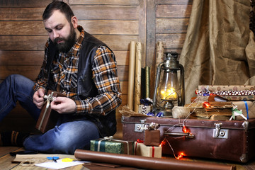 bearded man in shirt and vest packs Christmas gifts posing at camera