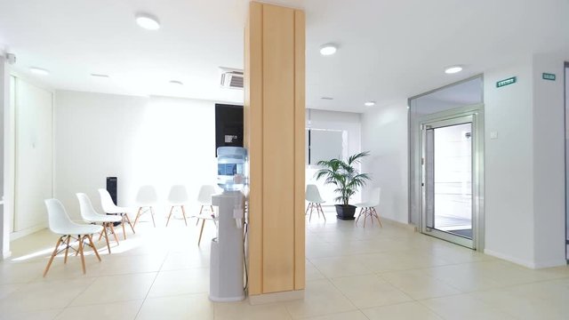 Panorama of a bright reception and waiting room in a clinic with desk, modern chairs and plants. 