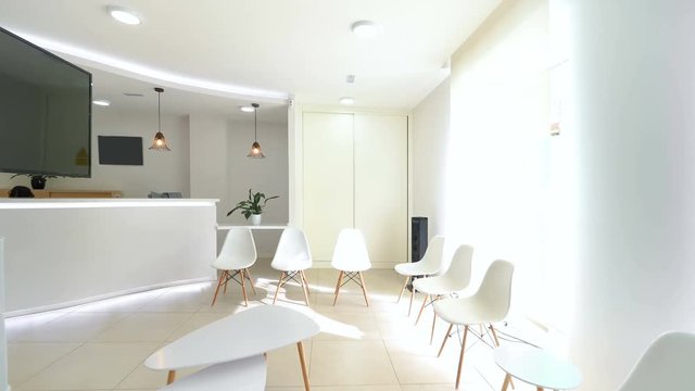 Panorama of a bright reception and waiting room in a clinic with desk, modern chairs and plants. 