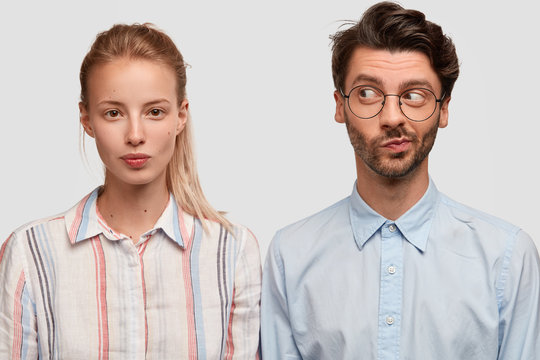 Indoor shot of friendly mixed race woman and man dressed in stylish shirts, pose together against white background, think about creative solution, collaborate for common task. Brother and sister