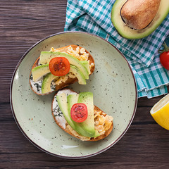 Toasts with avocado pieces, cherry tomatoes, scrambled eggs and soft cream cheese.