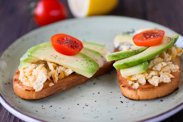 Toasts with avocado pieces, cherry tomatoes, scrambled eggs and soft cream cheese.