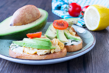 Toasts with avocado pieces, cherry tomatoes, scrambled eggs and soft cream cheese.