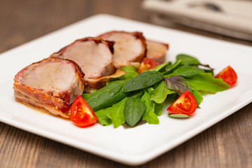 Fototapeta na wymiar Roasted Pork Tenderloin Wrapped in bacon with lettuce and tomatoes