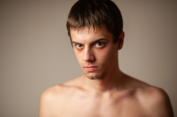 Studio shot of a young shirtless man over gray background. Man alone in the room