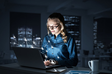 Attractive blonde wearing glasses in dark office using laptop. M