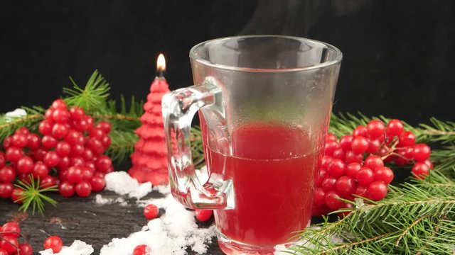 Winter still life with hot tea with viburnum berries on a wooden board with a burning candle and a pine branch covered with snow, black background