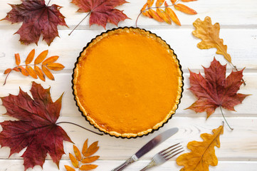 Homemade pumpkin pie on white wooden table with autumn leaves