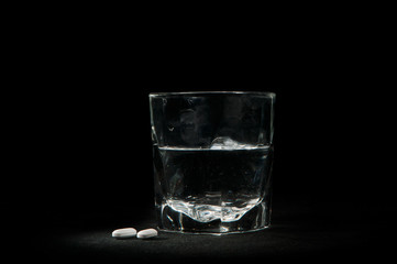 Glass of water and two pills on a black background