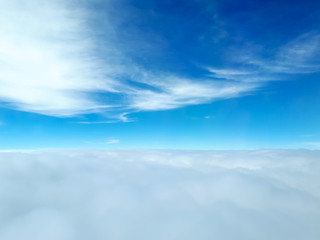 A wonderful view of many clouds from an airplane with a dense base of cumulus clouds in the bottom of the picture, a clear blue sky in the middle and few stratus clouds in the top