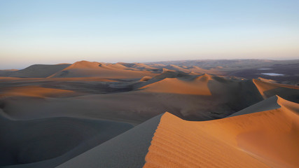 Fototapeta na wymiar Huacachina is a desert oasis in the sand dunes of Peru. It's 6pm and I'am sitting atop a giant wind-sculpted sand dune watching the sun set.
