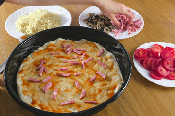 Making a pizza. Woman's hands make a homemade pizza. Putting ingredients.