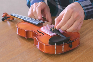 Close-up hands of young man in plaid shirt is repairing a violin sitting at the table. Tightens the bolts into place. © familylifestyle