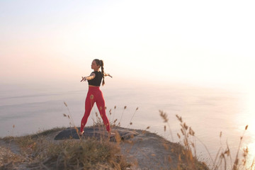 Beautiful view of woman doing yoga stretching on the mountain with sea view at sunset.