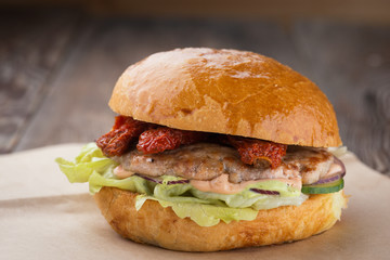 Homemade cheese burger or hamburger on brown paper put on wood table with copy space. Fast food for breakfast or lunch. Hamburger with dried tomatoes