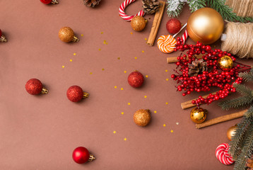 spruce branch, red and Golden Christmas balls, cones, cinnamon sticks, sweets on a brown background, a branch with red berries,