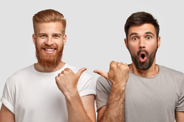 Shocked unshaven man with dark stubble indicates at his companion, wears grey t shirt. Cheerful...
