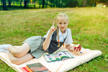 portrait of schoolgirl teenager with pigtails sitting in park on coverlet with apple