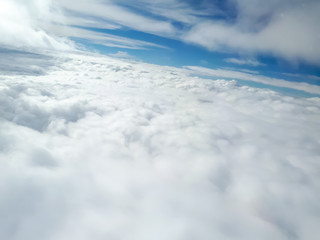 Fototapeta premium A nice aslope view of many clouds from an airplane with a dense and wide base of cumulus clouds in the bottom of the picture, a clear blue sky in the middle and few stratus clouds in the top