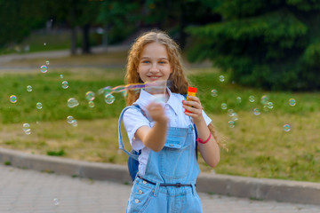 blond girl with curly hairstyle in denim overalls happy smiling blows soap bubble