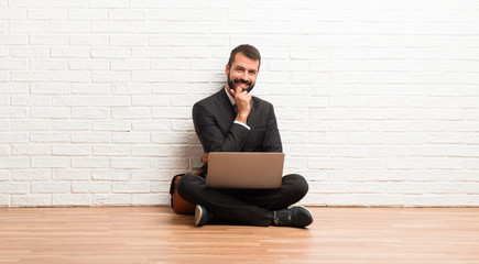 Businessman with his laptop sitting on the floor smiling with a sweet expression