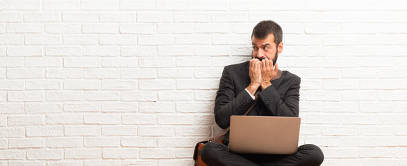 Businessman with his laptop sitting on the floor is a little bit nervous and scared putting hands...