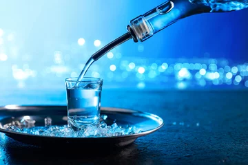 Fotobehang Bar Wodka gegoten in een glas verlicht met blauwe achtergrondverlichting.
