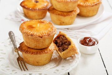 Traditional Australian Mini meat pies from shortbread dough on a white wooden background.