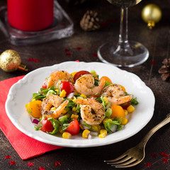 Salad with corn, fried shrimp, cherry tomatoes, red onions and lettuce on white plate. Appetizer for Christmas party