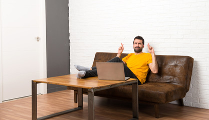 Man with his laptop in a room with fingers crossing and wishing the best