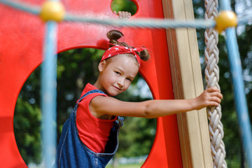 portrait of cute little girl in enim overall and  red T-shirt and  headscarf playing and having fun