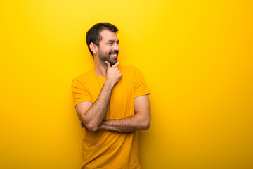 Fototapeta premium Man on isolated vibrant yellow color looking to the side with the hand on the chin