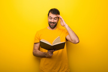 Man on isolated vibrant yellow color holding a book and surprised while enjoying reading