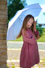 portrait of beautiful little girl. child in burgundy dress holds an umbrella over his head in bright sunny day