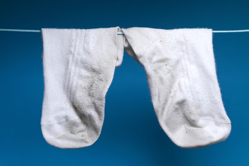two dirty white old sock weigh on the rope. blue background.