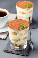 Traditional italian Tiramisu dessert cake in a glass, decorated with cocoa powder and mint, on gray background, vertical
