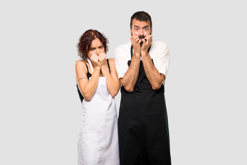 Couple of cooks is a little bit nervous and scared putting hands to mouth on grey background