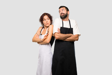 Couple of cooks making unimportant gesture while lifting the shoulders on grey background